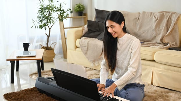 Smiling young woman practicing electric piano in her living room.