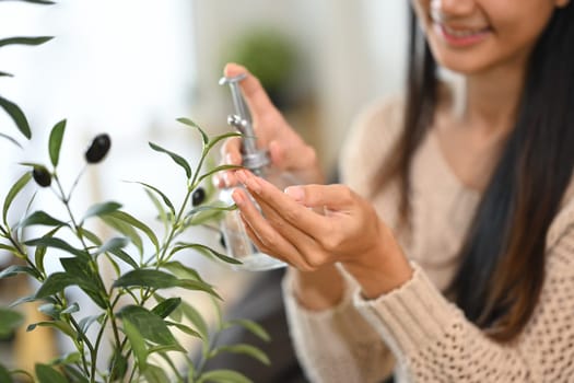 Beautiful young woman taking care and spraying water on houseplants with a bottle.