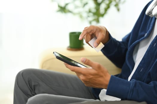 Young adult man holding a credit card and using smartphone for shopping online.