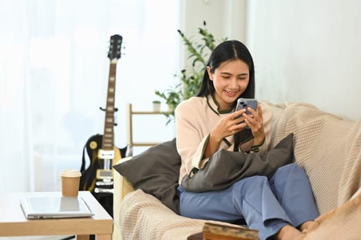 Happy young asian woman checking social media on smartphone at home.