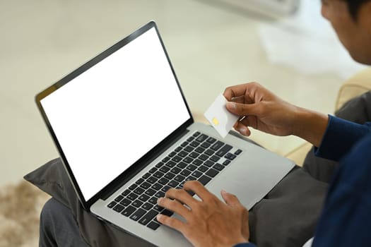 Young adult man holding a credit card and using laptop for shopping online.