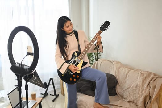 Young woman rocking out on electric guitar during live streaming or recording video.