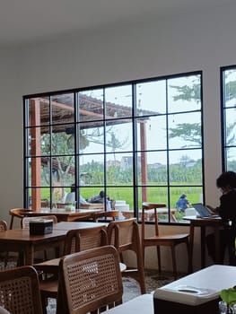 A cozy cafe interior featuring wooden furniture with a large window overlooking a serene garden. The peaceful atmosphere is ideal for relaxation and work.