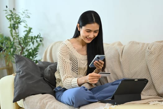 Charming young woman holding a credit card and using smartphone for shopping online.