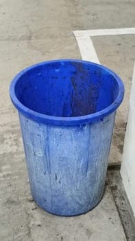 A lone blue plastic trash bin stands in an empty parking garage. The concrete surroundings create a stark, urban atmosphere. Ideal for themes of waste management and urban living.