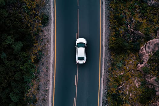 An aerial view captures a white car driving along an open road surrounded by scenic nature, highlighting the sense of freedom and adventure on a journey.