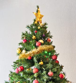 Golden star and colourful balls with color electtric lights decorating top of artificial Christmas tree.