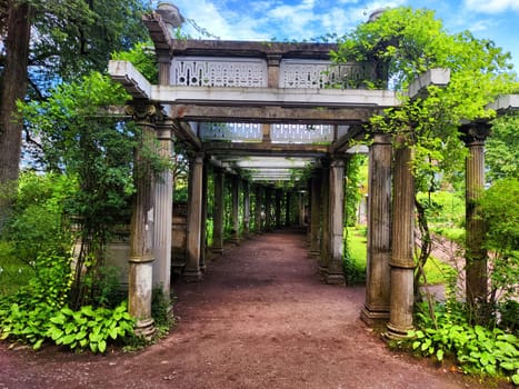 A tranquil walkway lined with greenery and ornate columns invites visitors into the garden.