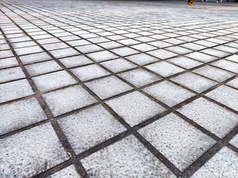 Textured gray tiles create a pattern on a city pavement in natural light.