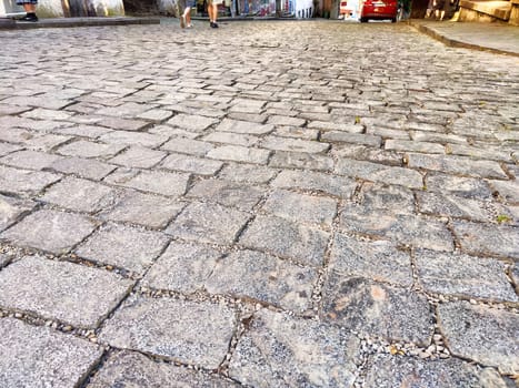 People stroll along a textured cobblestone street in a charming, historic area at dusk.