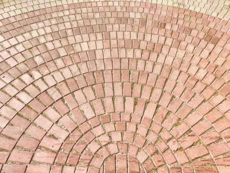 The ground is covered with a detailed arrangement of red bricks creating a circular pattern under the sunlight.