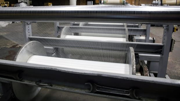 An industrial knitting machine in a textile factory with spools of white thread on a production line. Weaving fabric from yarn in a clean, well-lit manufacturing environment.