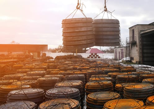 A crane hoists large, circular metal plates at an industrial site. Surrounding stacks of rusty plates indicate ongoing construction during overcast weather.
