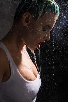 Sexy blonde in top staying under water pouring on her from above in the dark room profile portrait