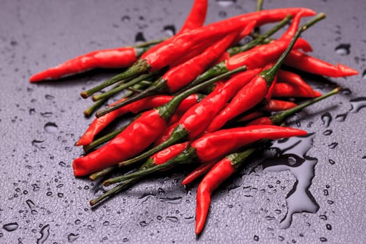 A close up photo of wet spicy red peppers on a black background.