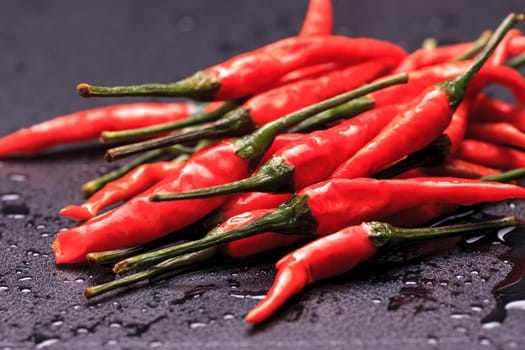 A close up photo of wet spicy red peppers on a black background.