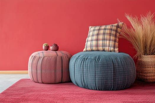 A stylish living area featuring round poufs in pink and blue, a plaid cushion resting on one, and decorative plants beside a textured basket against a red wall.