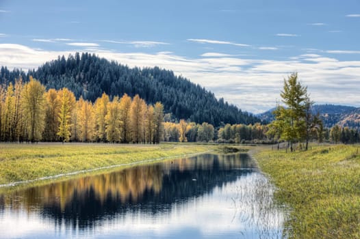 Calm water of the canal reflects the clouds in the partly blue sky on an autumn day near Bonners Ferry, Idaho.