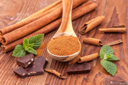Cinnamon powder on a wooden spoon, mint leaves, cinnamon sticks, and chunks of dark chocolate.
