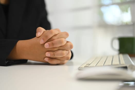 Close up of businesswoman in a suit with clasped hands sitting at a desk.