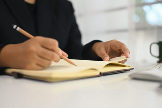 Close up view of businesswoman writing in a journal to remember a task or plan for a corporate project.