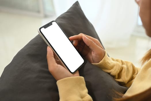 Woman hands holding smartphone with white empty screen sitting on sofa.
