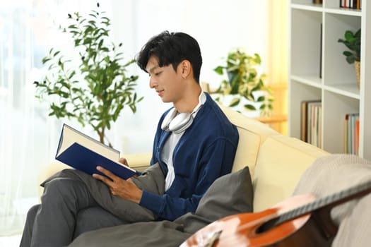 Casual young asian man enjoying a book while relaxing at home.