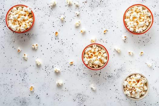 Four bowls of popcorn sit on a textured surface, surrounded by scattered kernels. This casual snack arrangement invites sharing during movie nights.