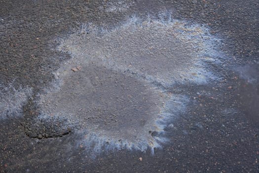 Oil stains on wet asphalt. Puddles are contaminated with multicolored streams of oil