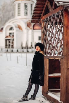 A beautiful woman in a black fur coat and a black hat has a lot of snow in winter, she is wearing red lipstick, smiling.