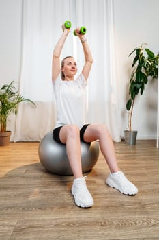 Woman exercising with dumbbells on a stability ball in a bright indoor space