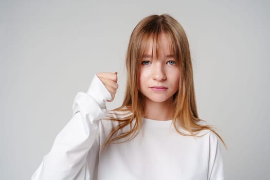 Young woman with long hair confidently raising her fist against a plain background close up