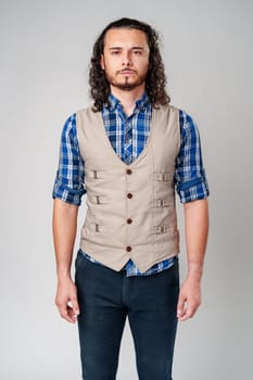 Young man in plaid shirt and vest poses confidently against a neutral background in a studio setting