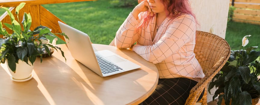 Woman working with laptop outdoor in summer terrace with black kitten. Girl and cat watching video on computer in the evening. Working from home, business, pet and lifestyle