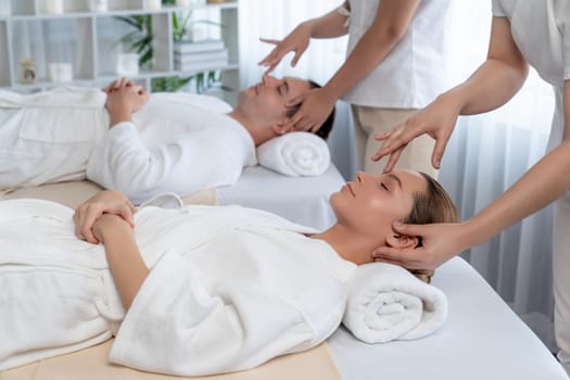 Caucasian couple enjoying relaxing anti-stress head massage and pampering facial beauty skin recreation leisure in dayspa modern light ambient at luxury resort or hotel spa salon. Quiescent