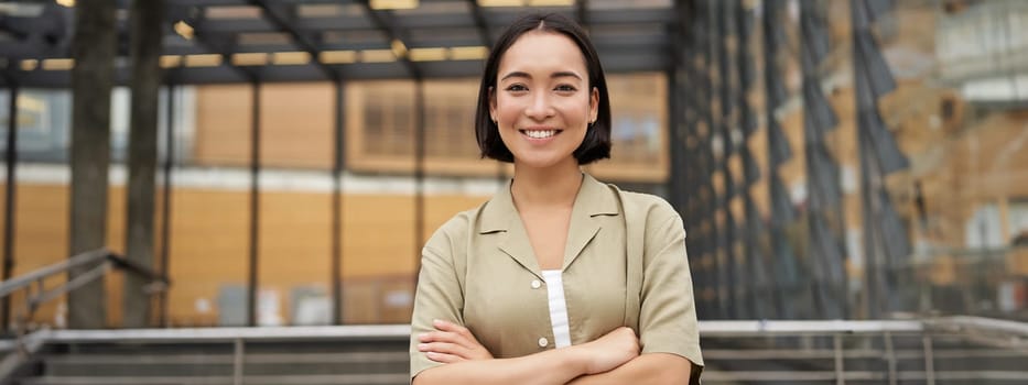 People. Portrait of confident korean girl, young student cross arms on chest, standing in power pose and smiling at camera.