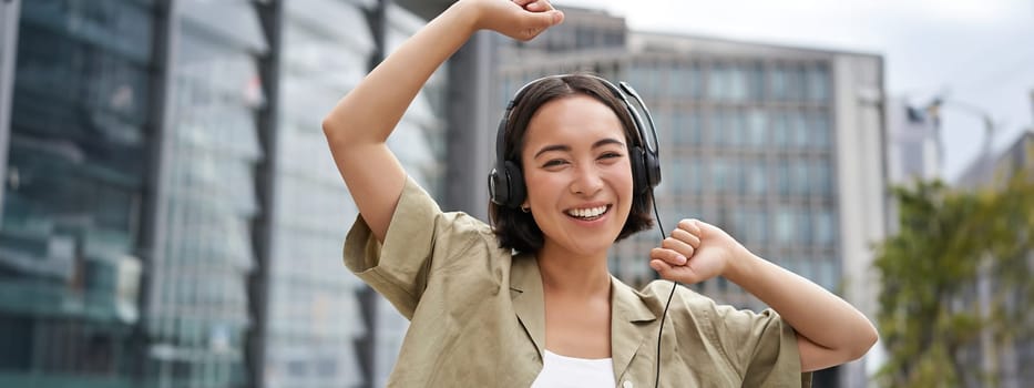 Girl dances on street with headphones on, listens to music and feels happy walking in city.