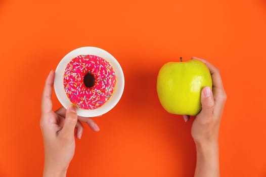Hands showing an apple and a donut as a healthy lifestyle concept. Young woman choosing between green apple or junk food, donut.