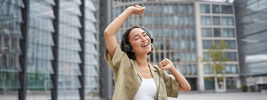 Girl dances on street with headphones on, listens to music and feels happy walking in city.