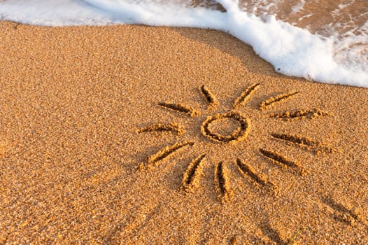 Soft waves with foam roll onto a golden sunny sandy beach at a resort during summer vacation. Symbol of the sun drawn on the sand.