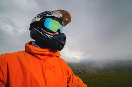 Portrait of a man in a protective sports helmet and reflective glasses. An athlete in full face in the mountains looks to the side.