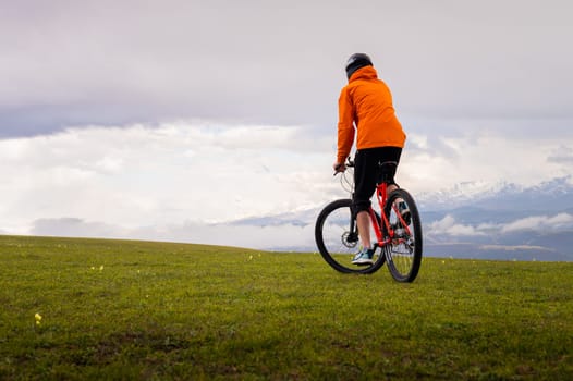 The cyclist rides in the mountains among the flowering fields. Cycling tour in nature. Extreme outdoor sports. Active happy healthy lifestyle.