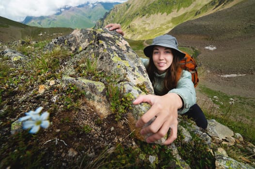 A brave young woman fearlessly climbs a steep stone wall in the mountains, overcoming obstacles. Adrenaline and courage in hiking, smiling girl with backpack climbs mountain