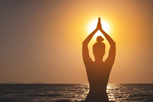 Rear view, silhouette of a woman holding the sun at dawn. a girl raising her hands, praying for God's blessings in the light of sunset or sunrise, practicing yoga on the beach, the concept of religion, freedom and spirituality.