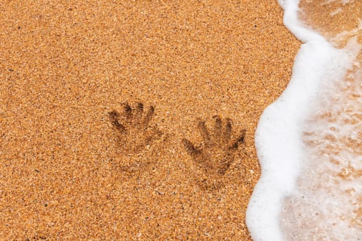 human traces of two hand prints on a sandy beach without people, sea waves rolling in from the side.