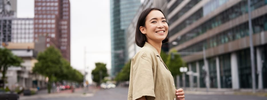 Outdoor shot of asian girl with laptop, going somewhere in city centre, walking on street, going to work.