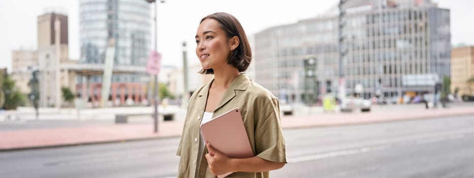 Portrait of young stylish woman walking with tablet, going somewhere in city.