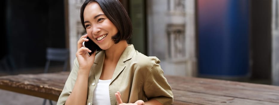 Young woman having conversation on mobile phone, sitting outdoors and making phone call, using smartphone, talking.