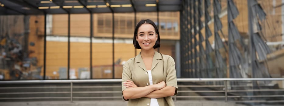 People. Portrait of confident korean girl, young student cross arms on chest, standing in power pose and smiling at camera.