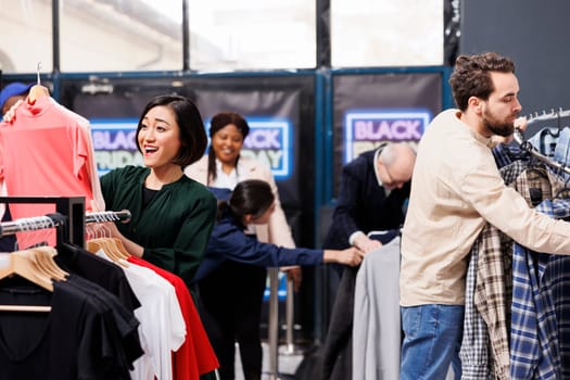 Seasonal sale at clothing store. Happy excited Black Friday shoppers grabbing clothes at discounted prices, hunting for bargains. Diverse people customers enjoying shopping at fashion outlet